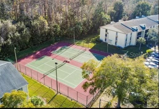 view of tennis court featuring fence, a forest view, and a lawn