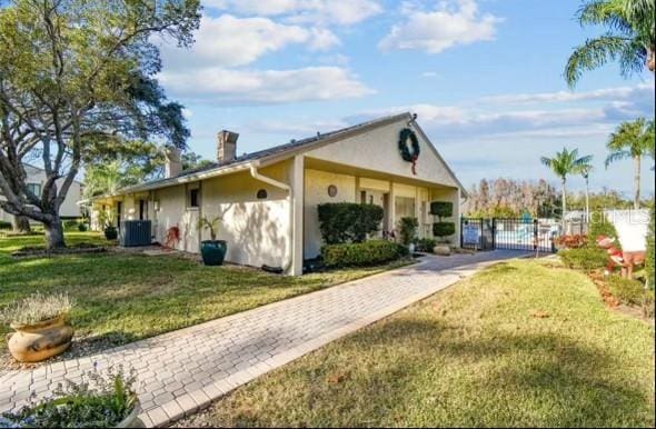 view of side of home with a yard, a chimney, stucco siding, central AC unit, and a gate