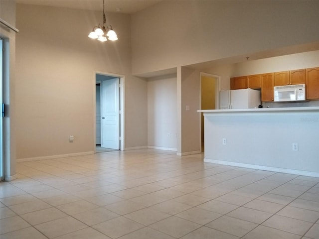 kitchen with light tile patterned flooring, a towering ceiling, a notable chandelier, and white appliances