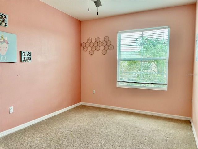 carpeted spare room featuring baseboards and a ceiling fan