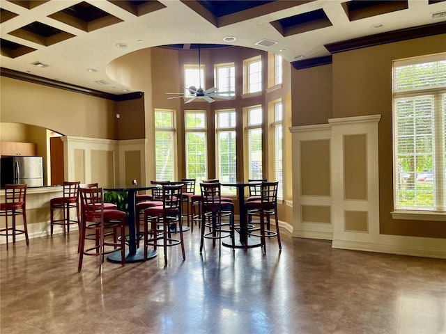 dining area featuring baseboards, arched walkways, a ceiling fan, ornamental molding, and a high ceiling