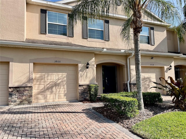 townhome / multi-family property with decorative driveway, a garage, stone siding, and stucco siding