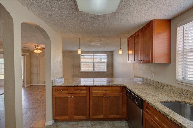 kitchen featuring kitchen peninsula, ceiling fan, hanging light fixtures, stainless steel dishwasher, and light stone counters