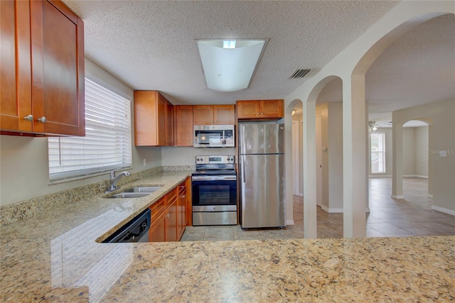 kitchen with light stone countertops, appliances with stainless steel finishes, sink, light tile patterned flooring, and ceiling fan