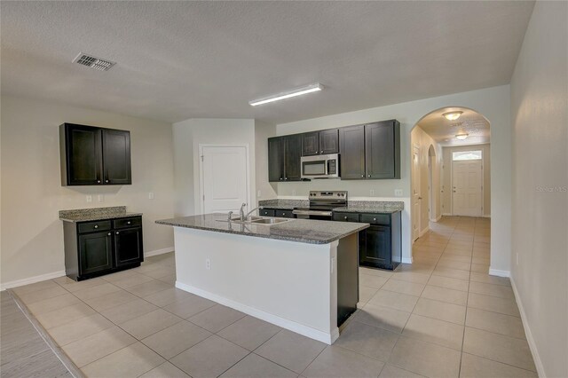 kitchen with light stone countertops, stainless steel appliances, an island with sink, sink, and light tile patterned floors