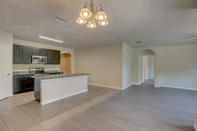 kitchen with appliances with stainless steel finishes, hanging light fixtures, a kitchen island with sink, a notable chandelier, and light tile patterned flooring