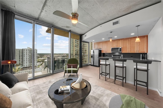 living room featuring visible vents, light wood-style flooring, ceiling fan, expansive windows, and a city view