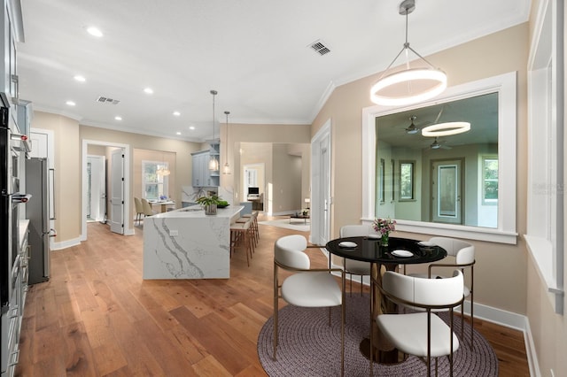 kitchen featuring pendant lighting, ceiling fan, ornamental molding, light hardwood / wood-style floors, and light stone counters