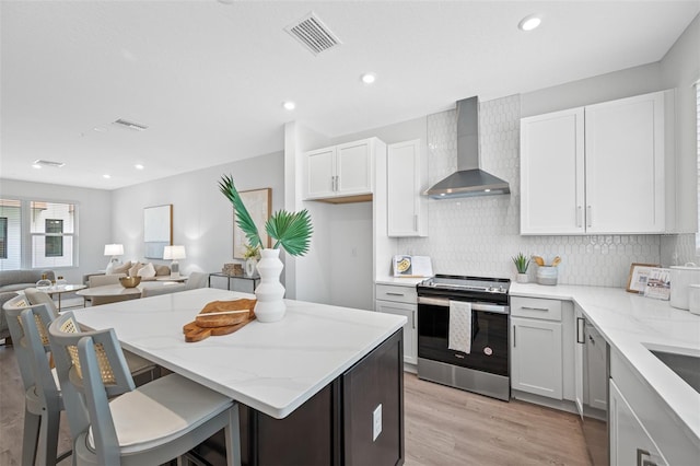 kitchen with a breakfast bar, backsplash, white cabinets, wall chimney range hood, and electric range