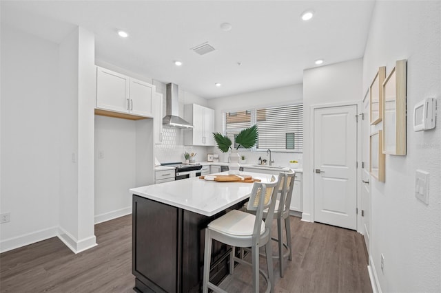 kitchen featuring wall chimney exhaust hood, electric range, white cabinets, a kitchen island, and a breakfast bar area