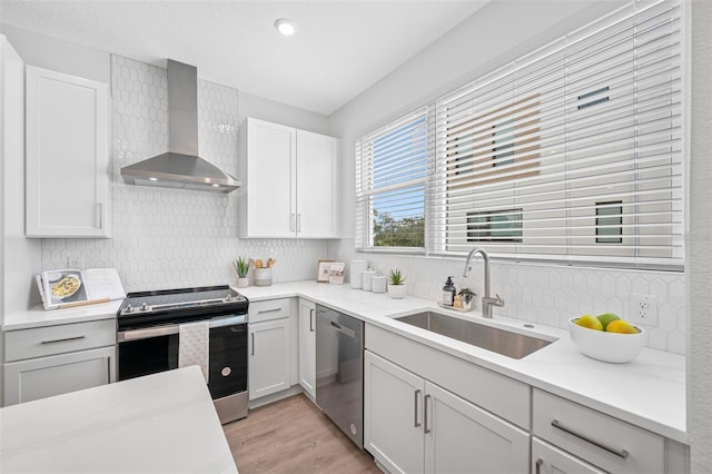 kitchen with appliances with stainless steel finishes, light wood-type flooring, backsplash, wall chimney exhaust hood, and sink