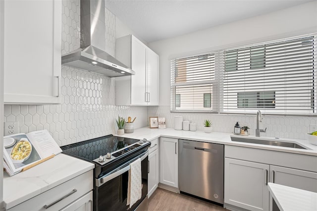 kitchen with sink, wall chimney exhaust hood, stainless steel appliances, tasteful backsplash, and light wood-type flooring