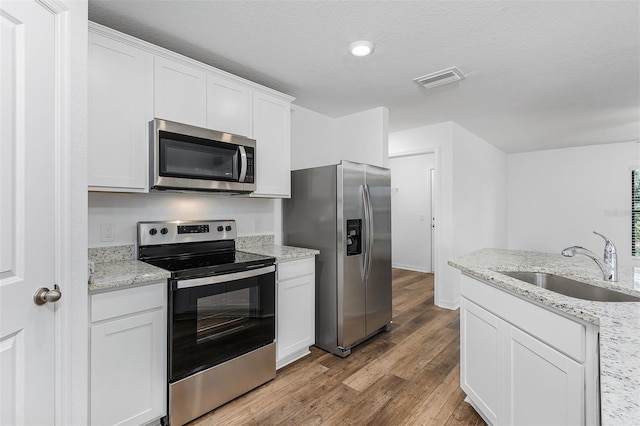 kitchen featuring sink, white cabinetry, stainless steel appliances, wood-type flooring, and light stone countertops