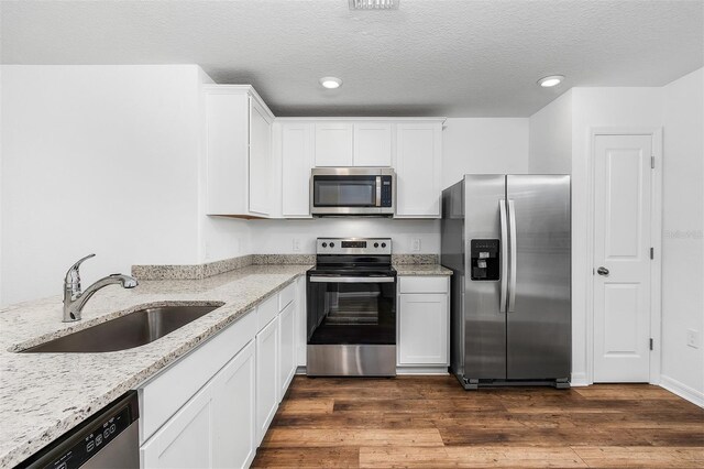 kitchen featuring dark hardwood / wood-style floors, stainless steel appliances, light stone counters, sink, and white cabinetry