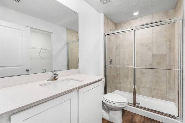 bathroom with hardwood / wood-style floors, a shower with door, a textured ceiling, toilet, and vanity