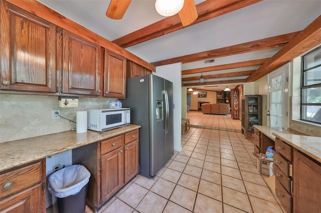 kitchen with light stone counters, light tile patterned floors, stainless steel fridge, and beamed ceiling