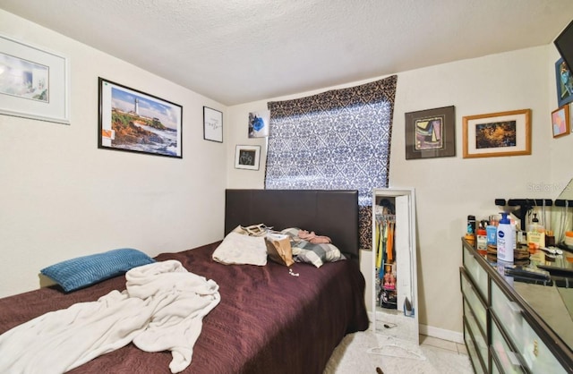 tiled bedroom with a walk in closet, a textured ceiling, and a closet