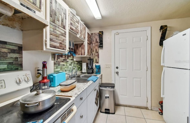 kitchen with sink, light tile patterned floors, a textured ceiling, white fridge, and range