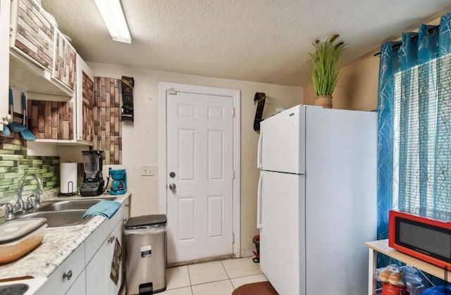 kitchen with white refrigerator, sink, light tile patterned floors, a textured ceiling, and white cabinetry