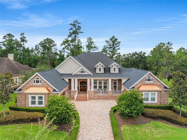 craftsman-style house with roof with shingles, a porch, decorative driveway, and brick siding