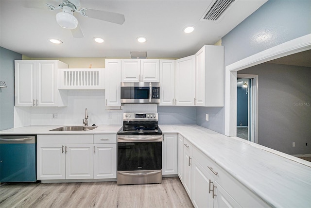 kitchen with appliances with stainless steel finishes, sink, light wood-type flooring, white cabinets, and ceiling fan