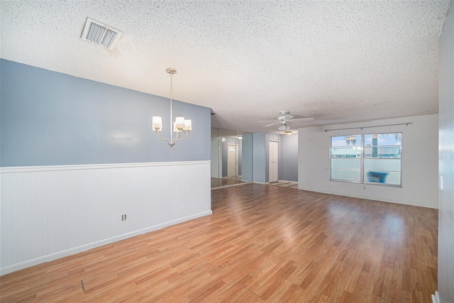 empty room featuring a textured ceiling, ceiling fan with notable chandelier, and wood-type flooring