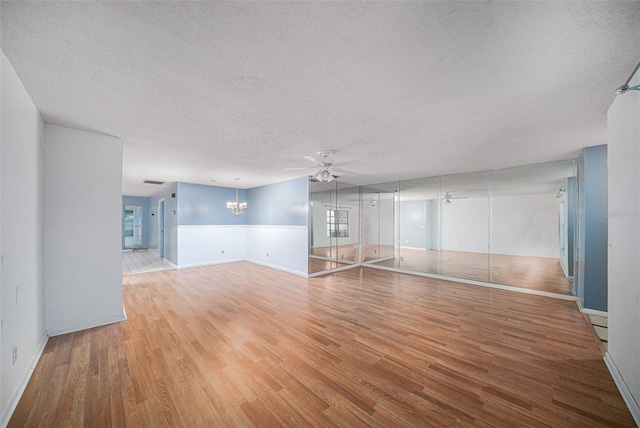 unfurnished living room with ceiling fan with notable chandelier, wood-type flooring, and a textured ceiling