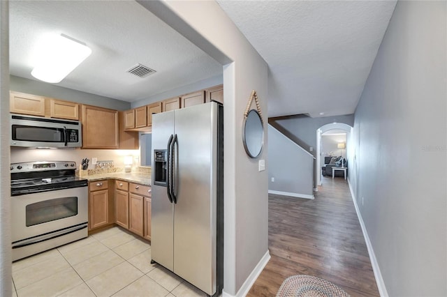 kitchen featuring light stone countertops, a textured ceiling, appliances with stainless steel finishes, and light hardwood / wood-style flooring