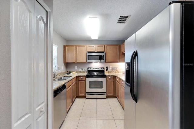 kitchen with light stone countertops, appliances with stainless steel finishes, a textured ceiling, sink, and light tile patterned floors