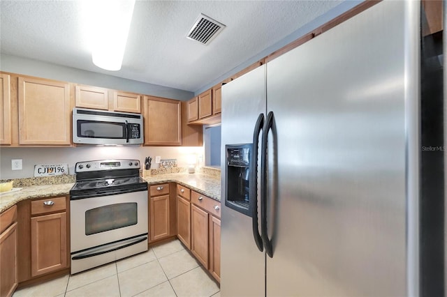 kitchen with light stone counters, light tile patterned floors, a textured ceiling, and appliances with stainless steel finishes