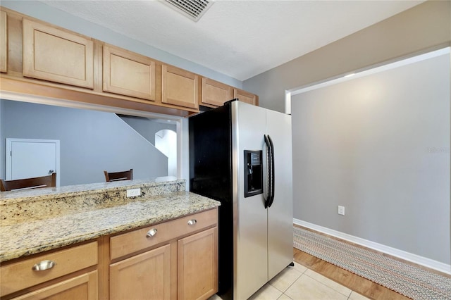 kitchen with stainless steel refrigerator with ice dispenser, light wood-type flooring, light stone counters, and light brown cabinets