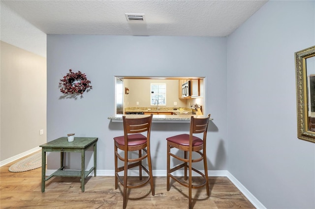 kitchen featuring light wood-type flooring, a textured ceiling, appliances with stainless steel finishes, light stone counters, and kitchen peninsula