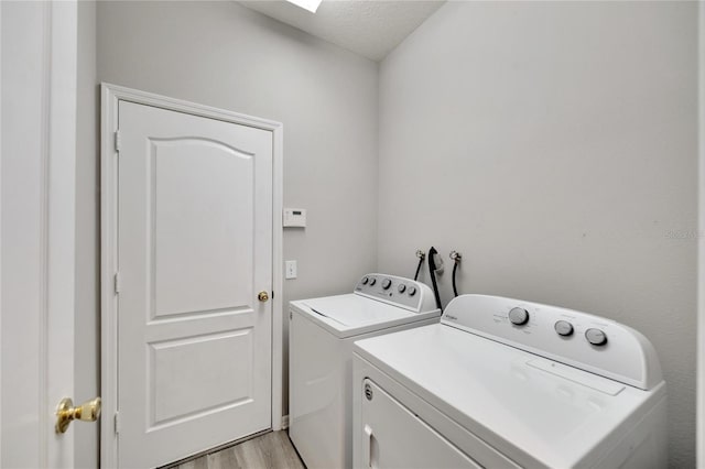 clothes washing area with a textured ceiling, separate washer and dryer, and light hardwood / wood-style floors