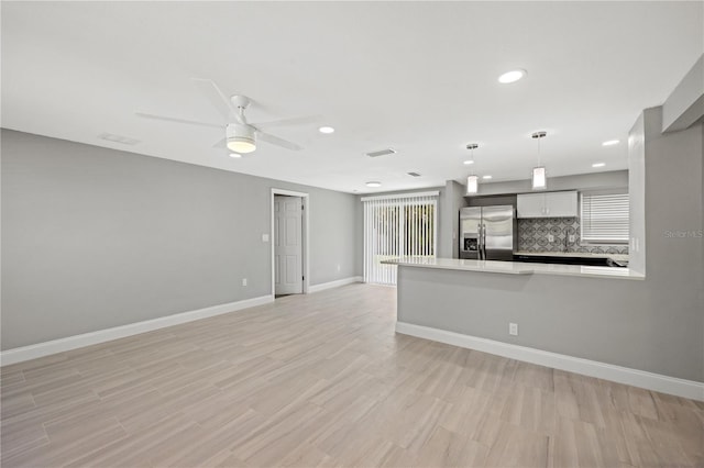 kitchen with decorative backsplash, stainless steel refrigerator with ice dispenser, kitchen peninsula, ceiling fan, and pendant lighting