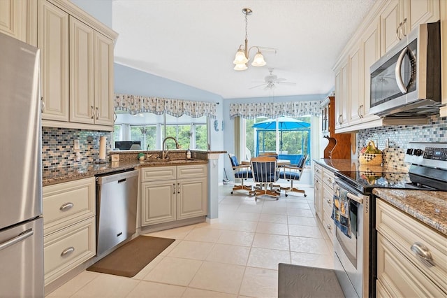 kitchen with light tile patterned floors, cream cabinets, a peninsula, a sink, and appliances with stainless steel finishes