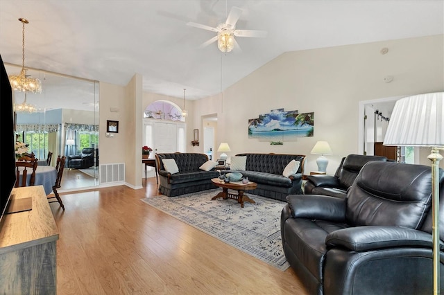 living area featuring ceiling fan with notable chandelier, lofted ceiling, visible vents, and wood finished floors