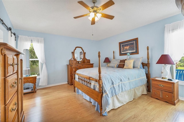 bedroom featuring multiple windows, a barn door, light wood-type flooring, and ceiling fan