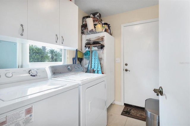 laundry area featuring light tile patterned floors, a textured ceiling, washing machine and clothes dryer, and cabinet space