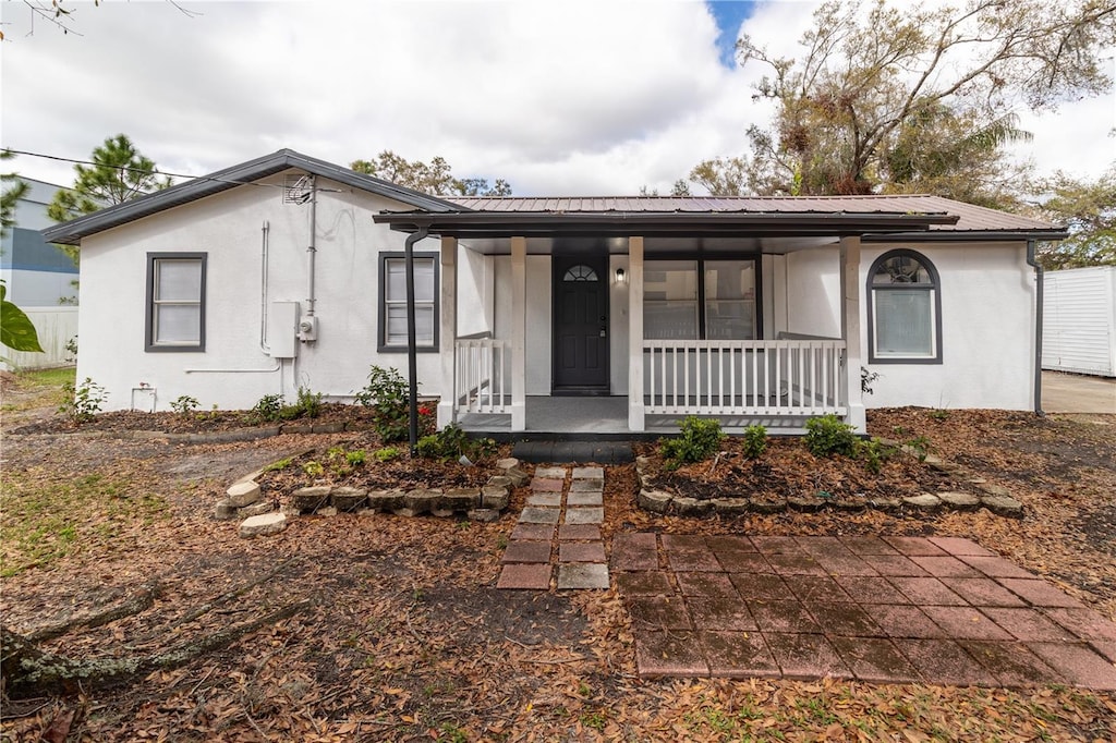 view of front of house featuring metal roof, a porch, and stucco siding