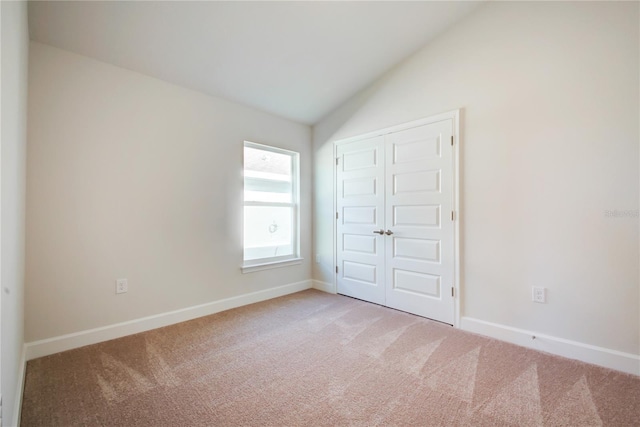 unfurnished bedroom with light colored carpet, lofted ceiling, and a closet