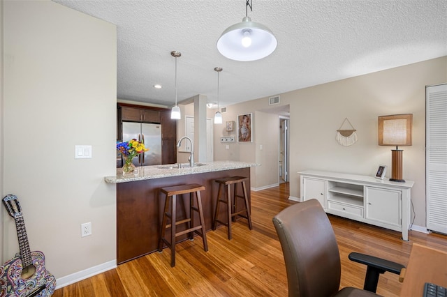 interior space with stainless steel refrigerator, sink, wood-type flooring, pendant lighting, and a breakfast bar