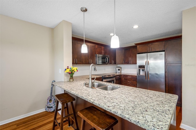 kitchen with a kitchen breakfast bar, dark hardwood / wood-style flooring, hanging light fixtures, stainless steel appliances, and kitchen peninsula