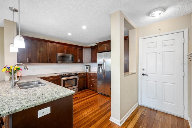 kitchen featuring pendant lighting, stainless steel appliances, dark hardwood / wood-style flooring, light stone counters, and sink