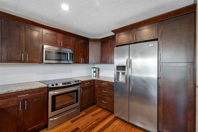 kitchen with backsplash, light stone countertops, stainless steel appliances, dark hardwood / wood-style flooring, and a textured ceiling