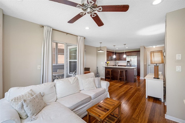 living room featuring a textured ceiling, dark wood-type flooring, and ceiling fan