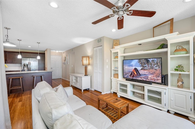 living room with ceiling fan, hardwood / wood-style flooring, and a textured ceiling