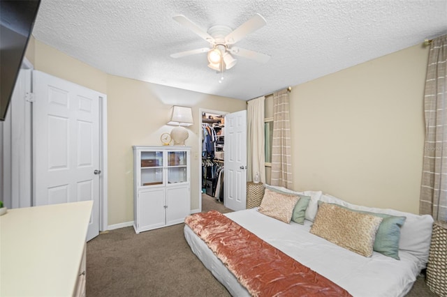 carpeted bedroom with a textured ceiling, a walk in closet, ceiling fan, and a closet