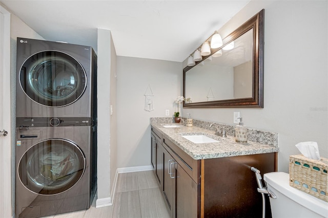 bathroom featuring stacked washer / dryer, toilet, vanity, and tile patterned flooring