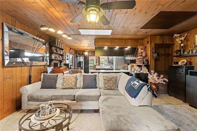 living room with a skylight, wooden ceiling, ceiling fan, and wood walls