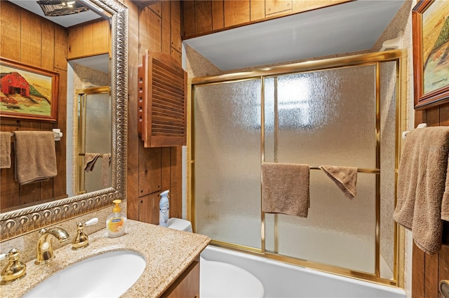 full bathroom with vanity, toilet, combined bath / shower with glass door, and wood walls